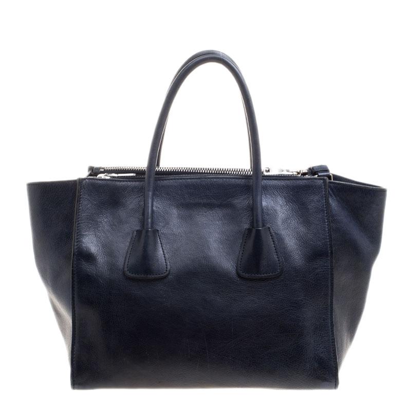 This elegant tote from Prada is crafted from leather and is perfect for daily use. The bag features double handles, an adjustable shoulder strap and protective metal feet at the bottom. The snap button closure opens to a nylon lined interior that
