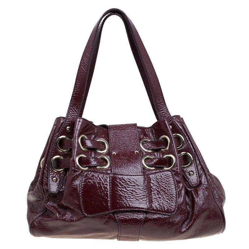 This riki tote has the perfect flavor of elegance and style and is a typical Jimmy Choo creation. Crafted from fine quality patent leather, the bag has a rich burgundy color. The front flap has a gold-colored buckle and the brand name embossed on a