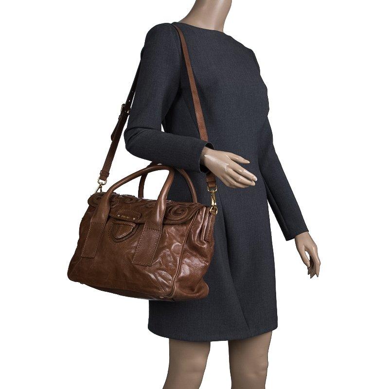 Crafted from glazed leather, this brown Prada bag has a push lock closure that opens to a suede-lined interior. The bag is equipped with dual rolled handles, a detachable shoulder strap, gold-tone hardware, and protective metal feet. Swing this