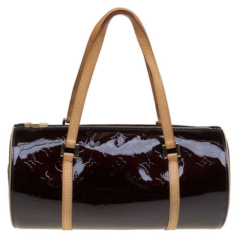 The bag is crafted from Amarante monogrammed Vernis leather with vachetta trim and shoulder straps. The exterior features a side pocket, top zip closure, and gold tone hardware. Its smooth leather lined interior is perfect for carrying essentials in