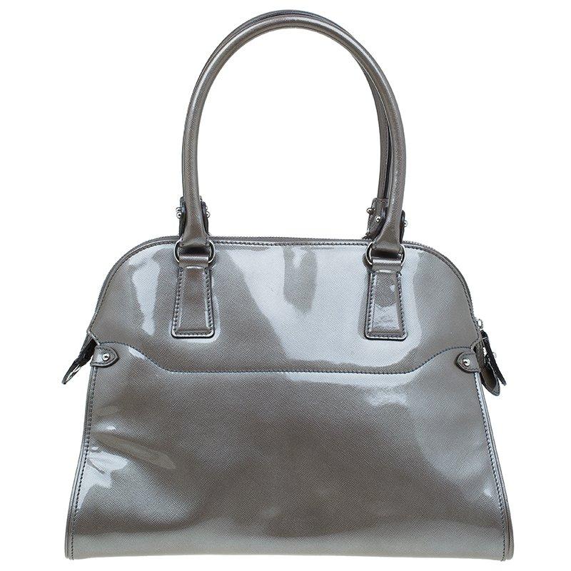 Crafted from smooth silver patent leather, this Salvatore Ferragamo satchel is the perfect everyday acquaintance. Its coupled with silver-tone Ferragamo buckle and hardware accents. It features double top rolled handles and a zip closure that opens