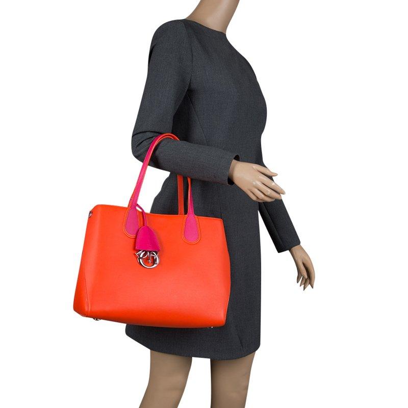 This shopping tote from Dior is a timeless piece. The bag is crafted from red orange leather and features dual handles, protective feet at the bottom and Dior letter charms. A top buttoned closure opens to a leather lined interior and the bag is
