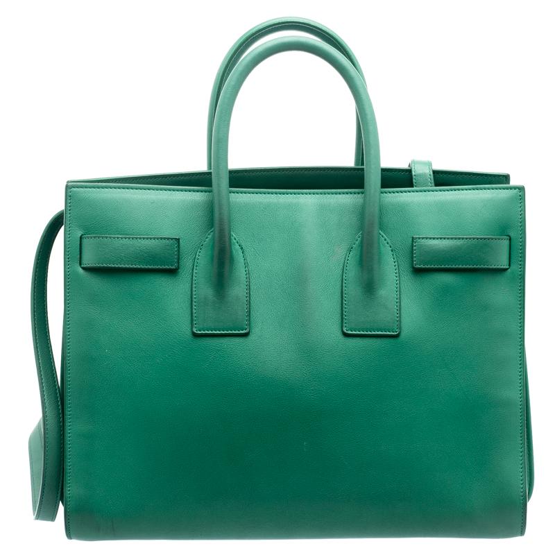 This Sac de Jour tote bag by Saint Laurent Paris has a sophisticated look. Crafted from green leather, the exterior features double top handles along with a shoulder strap. The tote comes with a suede lined interior that has two open compartments