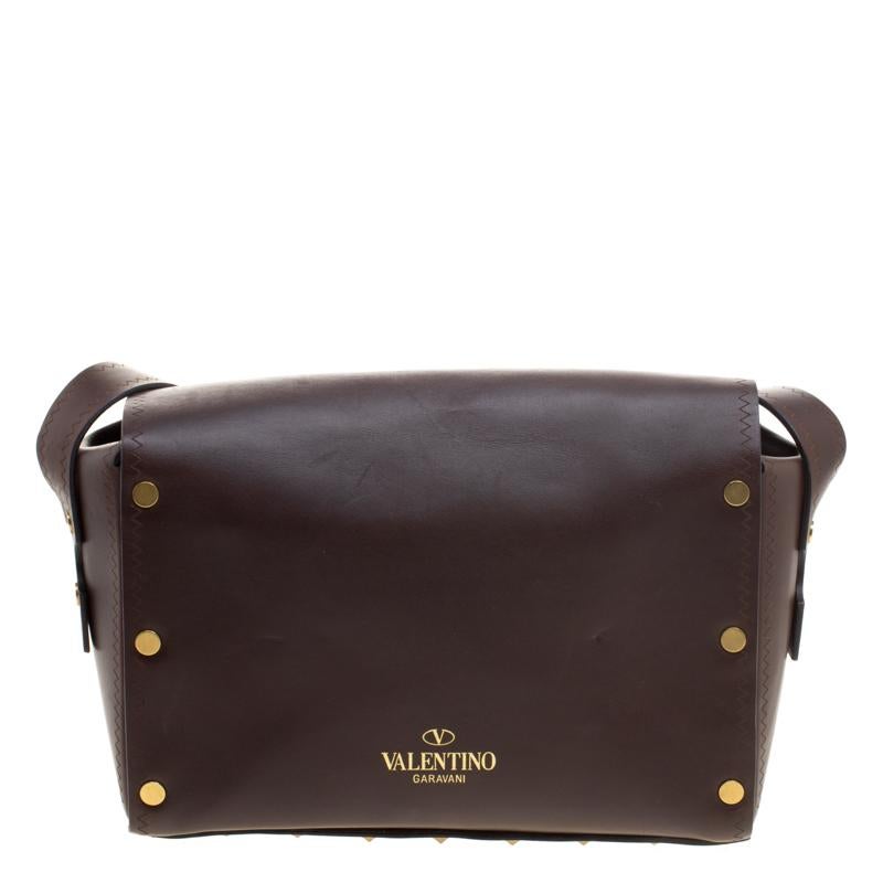 From the house of Valentino comes this gorgeous box bag that will perfectly complement all your outfits. It has been crafted from dark brown leather and styled with a flap. It has a combination of gold tone studs and tribal embellishments all over