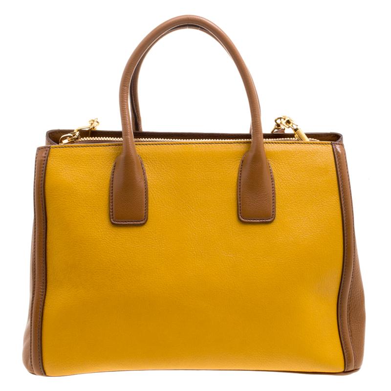 This Convertible tote from Miu Miu is sure to make heads turn. Crafted from yellow and brown leather, the bag features dual top handles, an adjustable shoulder strap, and protective metal feet. The bag opens to a spacious satin lined interior that