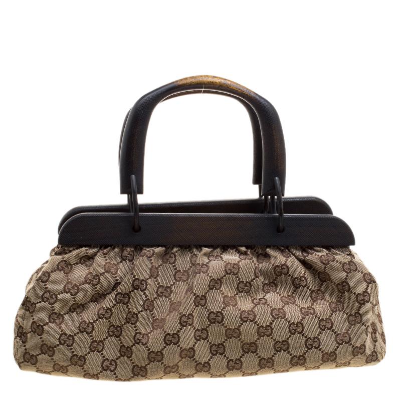 This Doctors bag from the house of Gucci features a sturdy wooden top and a beige canvas body with 'GG' web detail on it. It comes with two top handles and secured with a buckle closure. The fabric-lined interior can hold all your day to evening