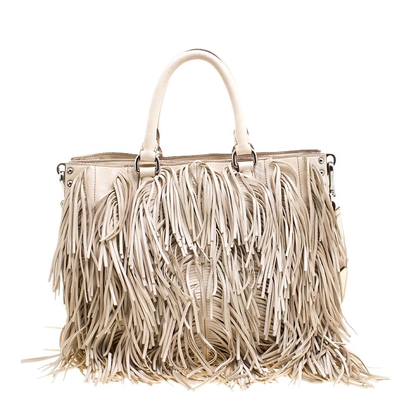 Designed in a large spacious tote size, this Prada bag is high on style as it is high on utility. Crafted in beige leather, this bag is accented with fringe details all through the front and the back of this bag along with silver tone stud details