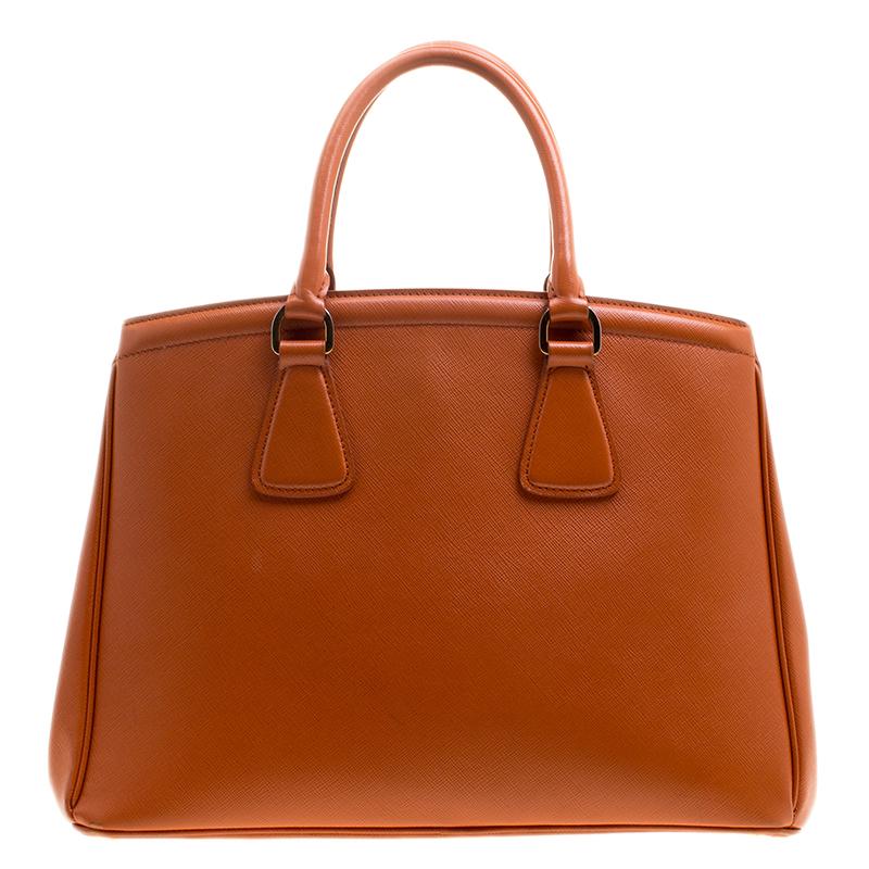 Prada’s Parabole tote is a statement piece that will uplift any outfit. It is made with Saffiano Lux leather in eye-popping orange hue which is further accented with the brand’s signature in gold-tone and a leather tag. The bag features dual handles