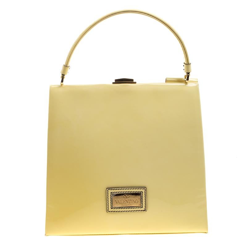 This tote is finely structured in huge box shape made from the pure shiny leather designed by Valentino. It has short rounded handle on the top that is closed with the metal buckle on the top. It is beautifully defined with a ruffled bow providing