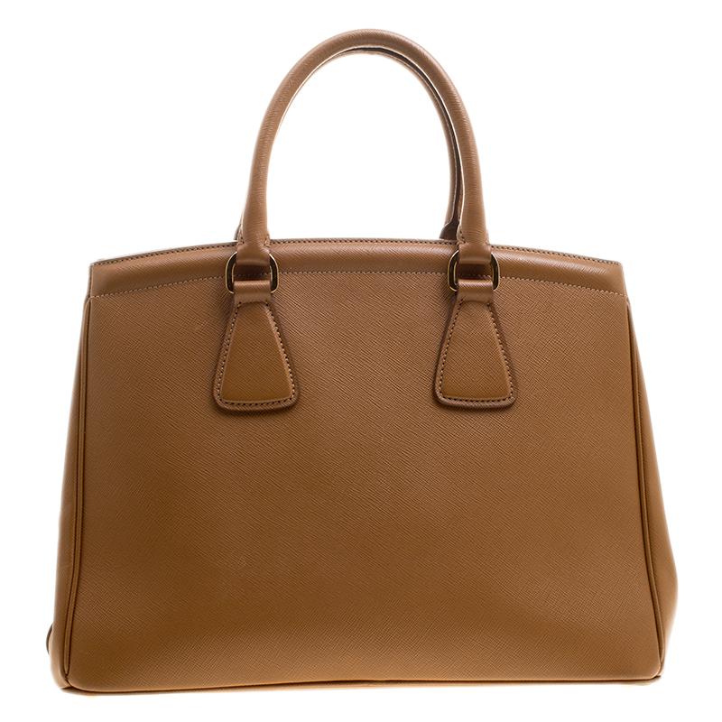 This sophisticated Parabole tote from Prada is crafted from Saffiano lux leather. The tote has a caramel exterior featuring dual handles, a leather tag and protective metal feet at the bottom. The nylon lined interior houses two open compartments