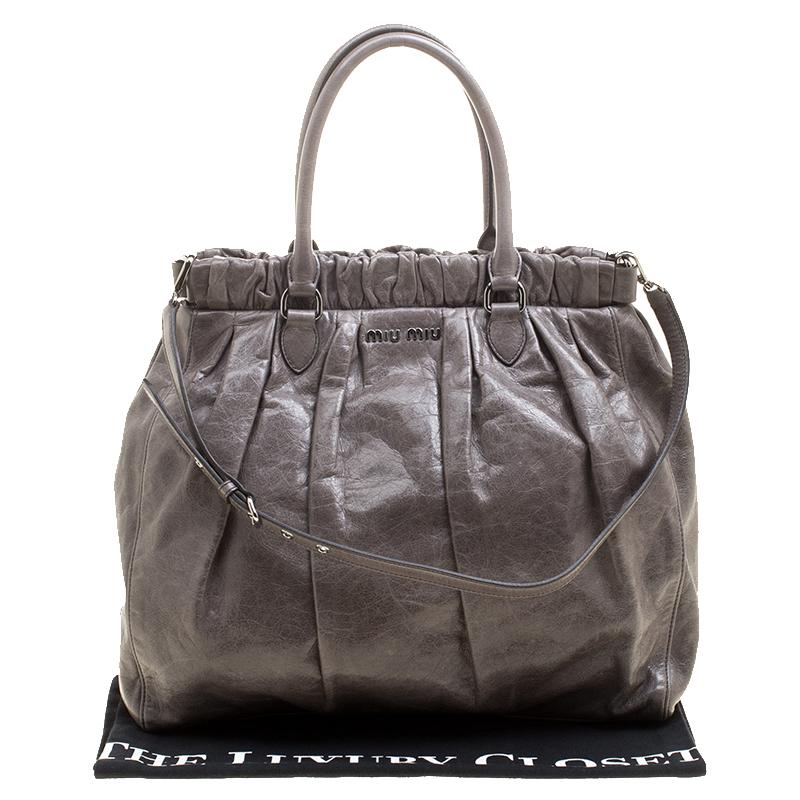 Displaying the brand's creativity and vision, this Miu Miu tote is crafted with lux leather in grey color. It is designed in an interesting gathered style and has dual top handles and an adjustable shoulder strap. The bag comes with a satin-lined