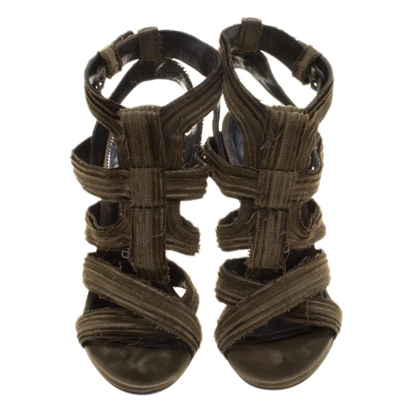 These stunning strap sandals from Tom Ford are sure to add an edgy and modern chic look to your party looks. Constructed in olive green satin with raw edge finish, these cross strap sandals go upto the ankle with a belted loop closure and peep toes