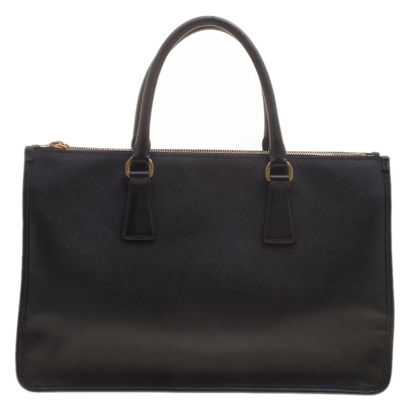 This structured handle bag by Prada is crafted from fine and exclusive Saffiano lux leather. The black colored bag features double rolled leather handles and a kiss-lock frame center compartment at the center for the safety of your valuables. It