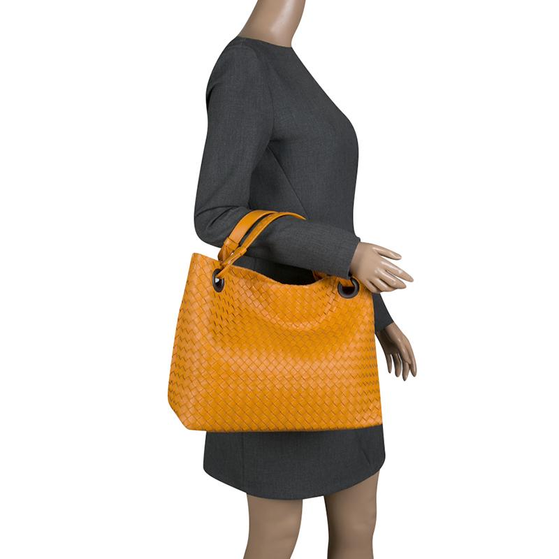 This tote from Bottega Veneta is spacious. Crafted from leather, it features double top flat handles, protective metal feet, and a capacious suede interior. The exterior of the bag with orange hue carries the famous Intrecciato pattern that is
