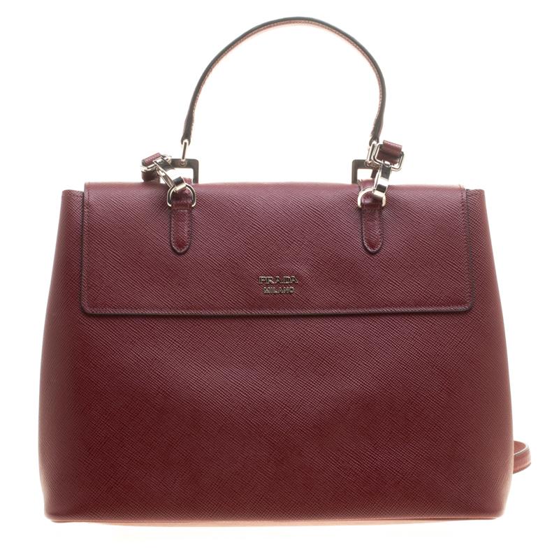 Prada is defined by its exalted craftsmanship, and this burgundy top handle bag is a true testimony of their flair. This bag is an elegant combination of style, sophistication, and structure. The Saffiano Lux leather exterior is paired with belt