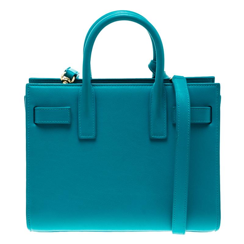 This Sac de Jour tote by Saint Laurent has a structure that simply spells sophistication. Crafted from turquoise leather, the bag is held by double top handles and a shoulder strap. The tote comes with a suede-lined interior with enough space to