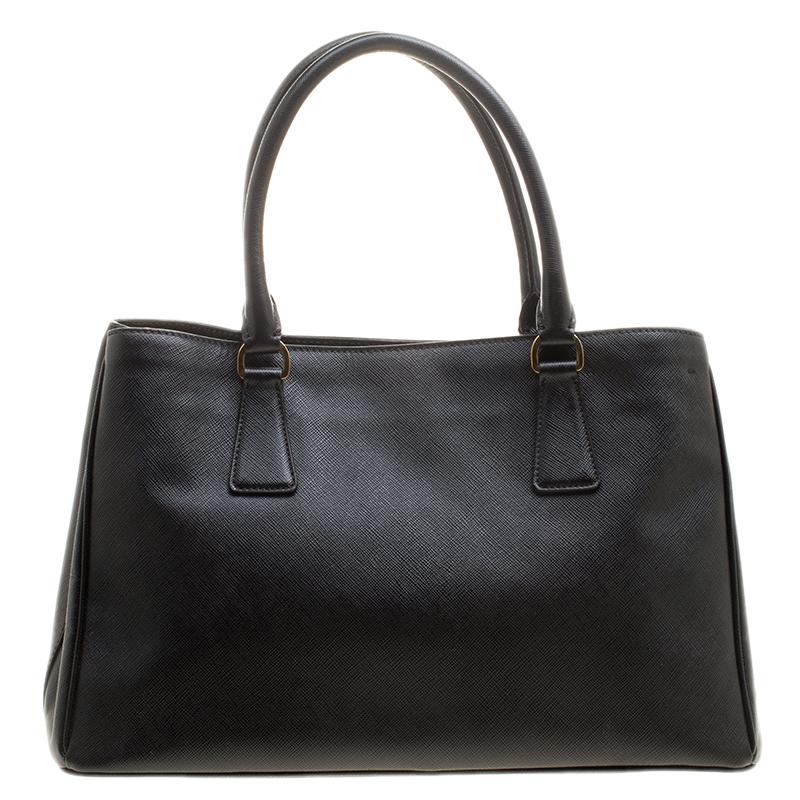 This elegant tote from Prada is crafted from Saffiano Lux leather and is perfect for daily use. The bag features double handles, a leather covered gold key ring, protective metal feet, and a removable shoulder strap. It has a nylon lined interior