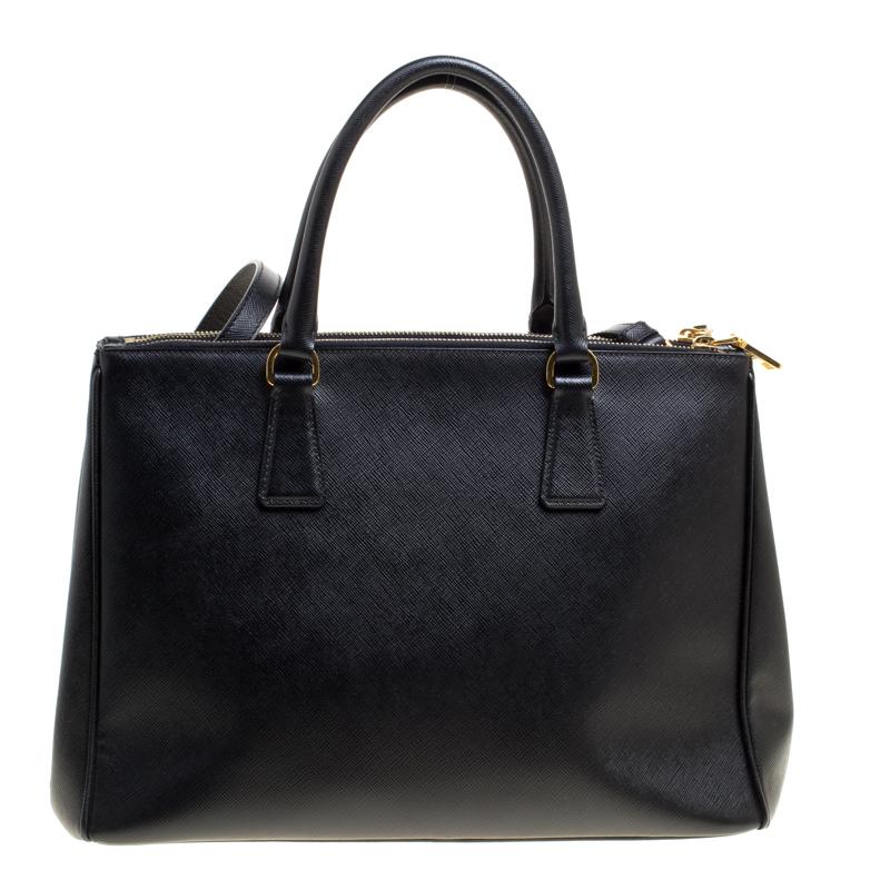 This elegant tote from Prada is crafted from Saffiano leather and is perfect for daily use. The bag features double handles, a leather covered gold key ring, detachable shoulder strap, and protective metal feet. It has a nylon lined interior that