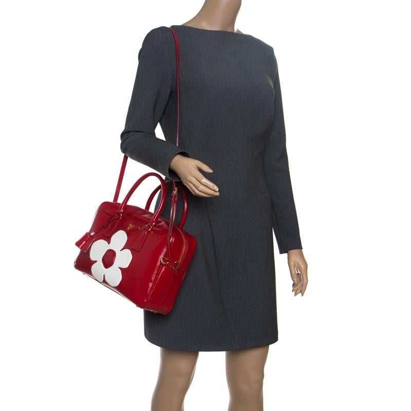 This rollicking red bag is up for grabs and is designed in a very stylish silhouette. It is made of saffiano Vernice patent leather. The white flower on it just simply cannot be ignored and the bag shines with the gold-tone hardware. Pair it with