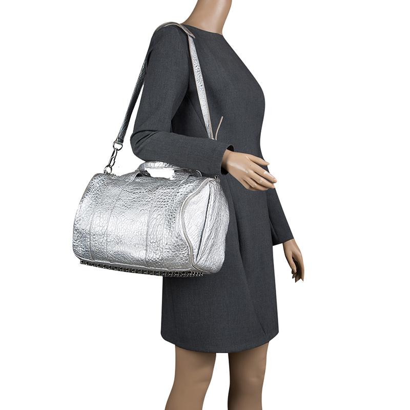 Creations like this Rocco Duffle Bag by Alexander Wang never go out of style. This silver bag is crafted from pebbled leather and it features dual handles, a detachable shoulder strap, and studs on the bottom. The top zipper opens to a fabric