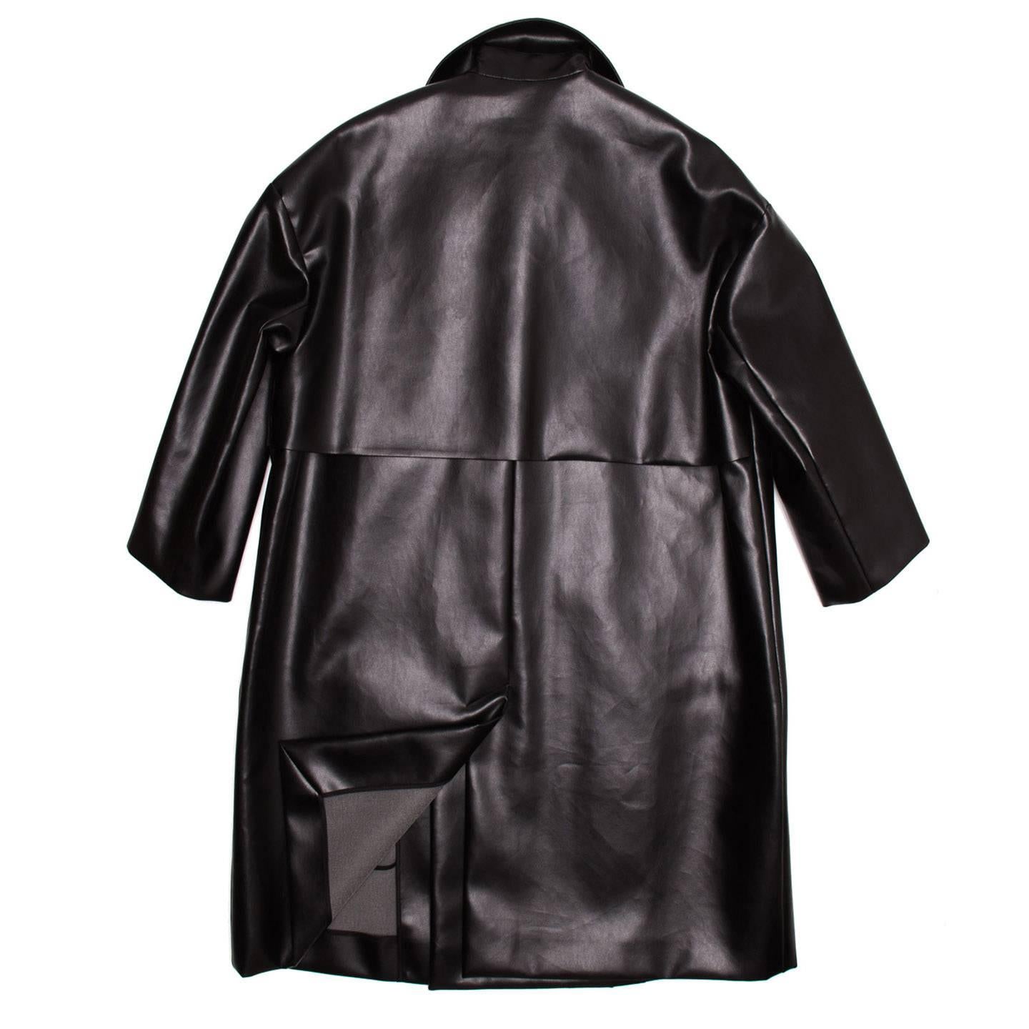Black oversized polyurethane coat with 3/4 sleeves. The coat is knee length, boxy fit and the front opening is buttonless. The lapel is quite wide, the trench coat typical yoke details embellish front and back and the two slit pockets sit at hips.