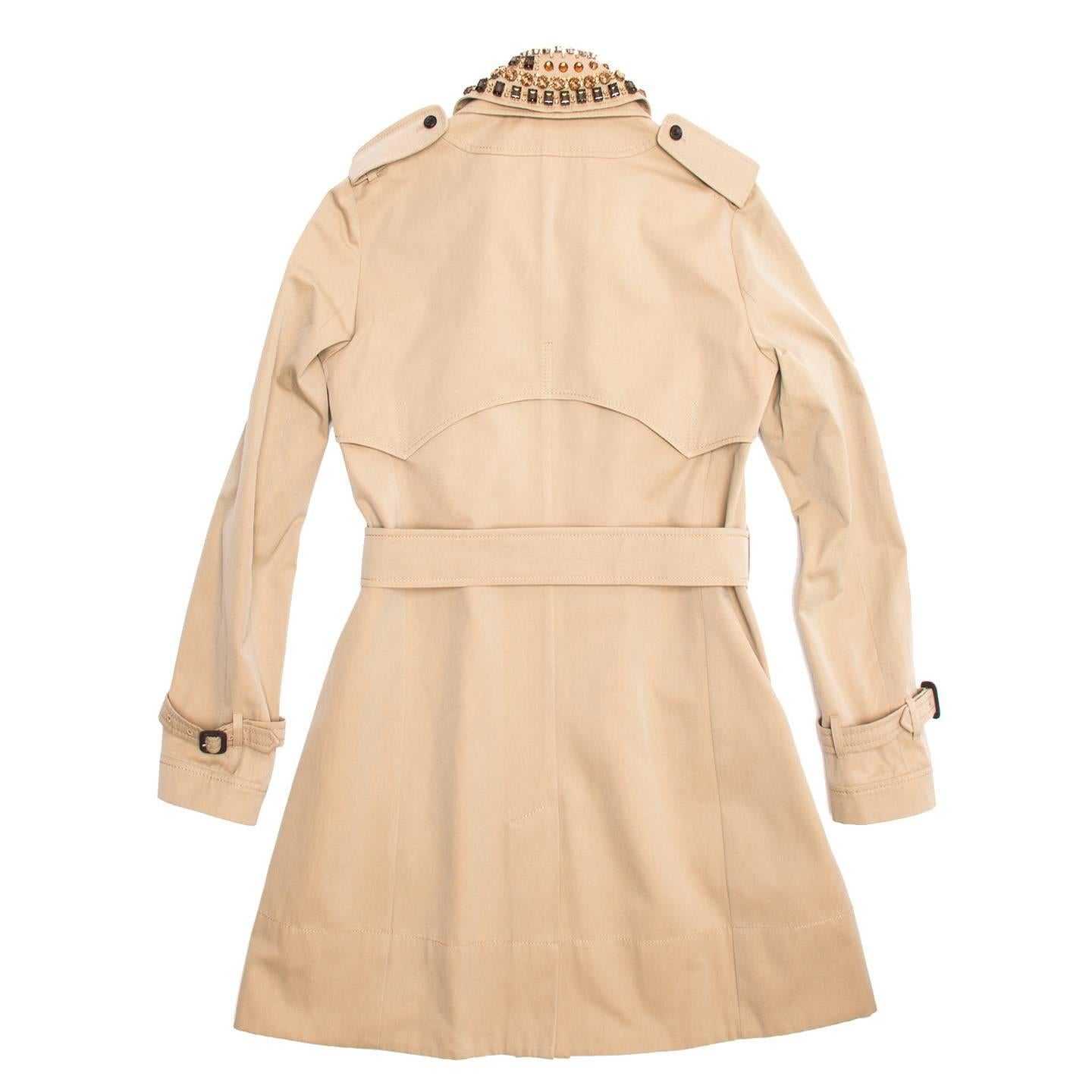Classic knee length khaki cotton trench coat with belted waist and detachable jewel embellished collar. The front is single breasted and fastens with brown buttons like the smaller ones on the pockets. The cuffs are belted as well and enriched with