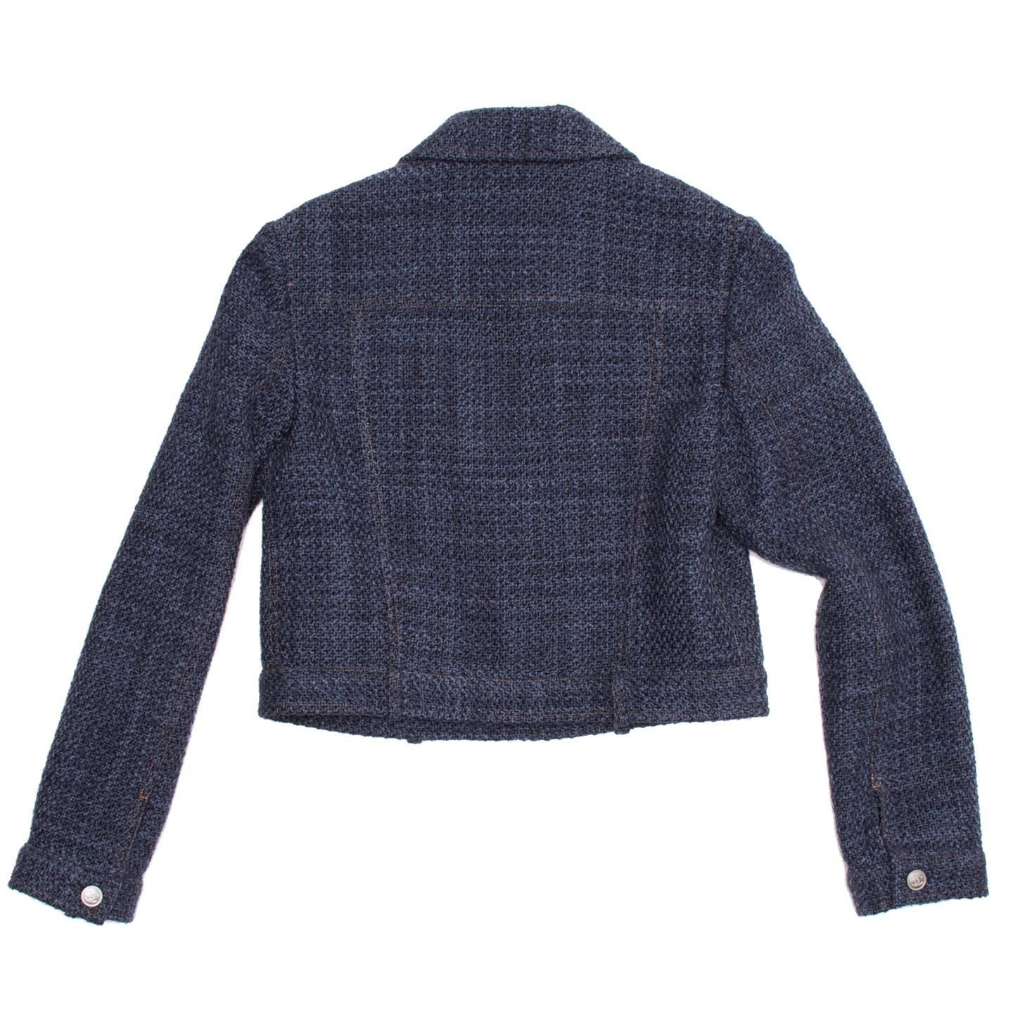 Indigo wool blend tweed cropped trucker style jacket with two patch pockets with flaps fastened by Chanel logo metal snap buttons. The same brushed silver metal buttons close the center front and the cuffs, while the hem is enriched by a jeans style