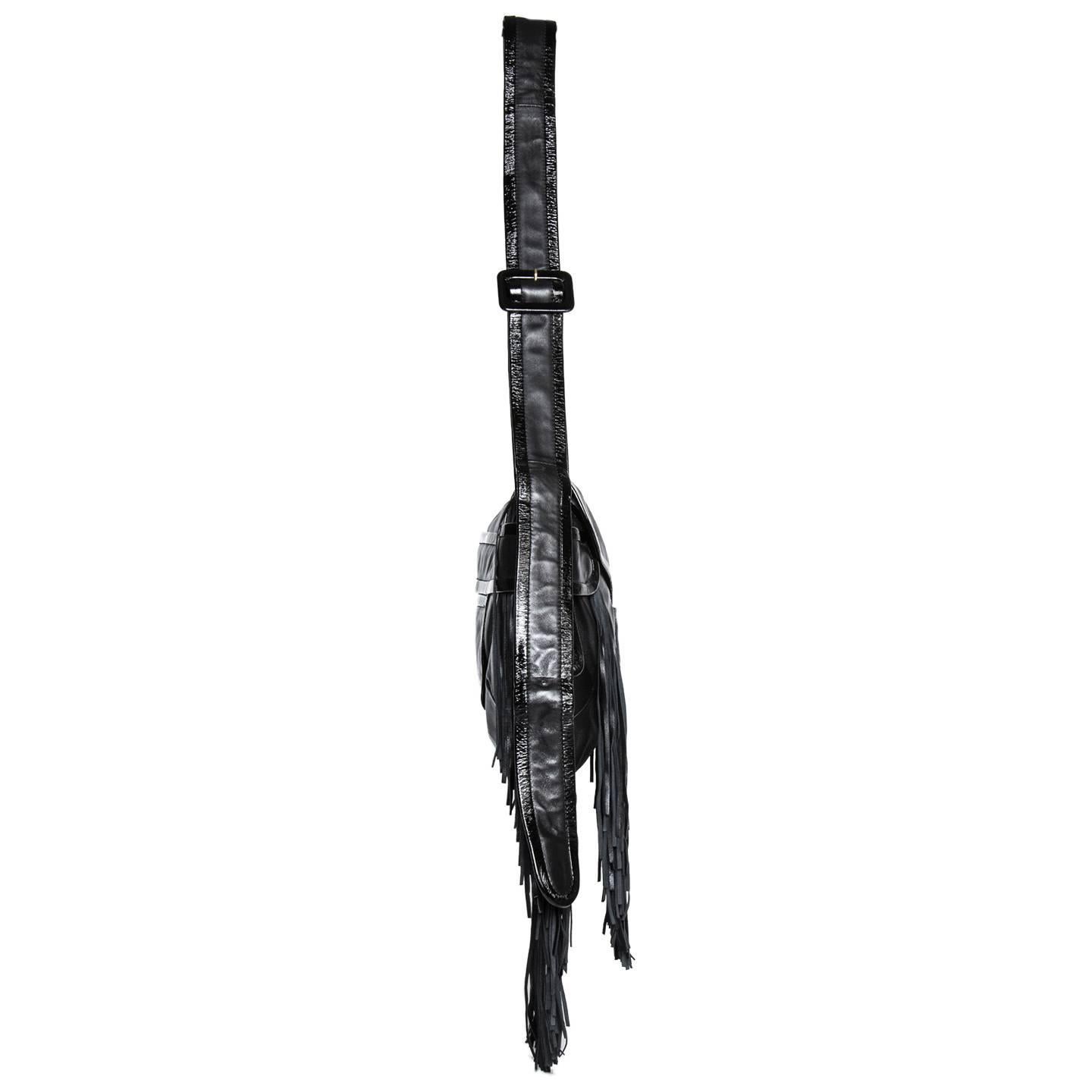 Black supple nappa leather bag with patent leather profiles and thin fringes at bottom and front. All the profiles are round as well as the flap that overlays at front into a slide detail, little patch pockets and thick straps at front and sides.