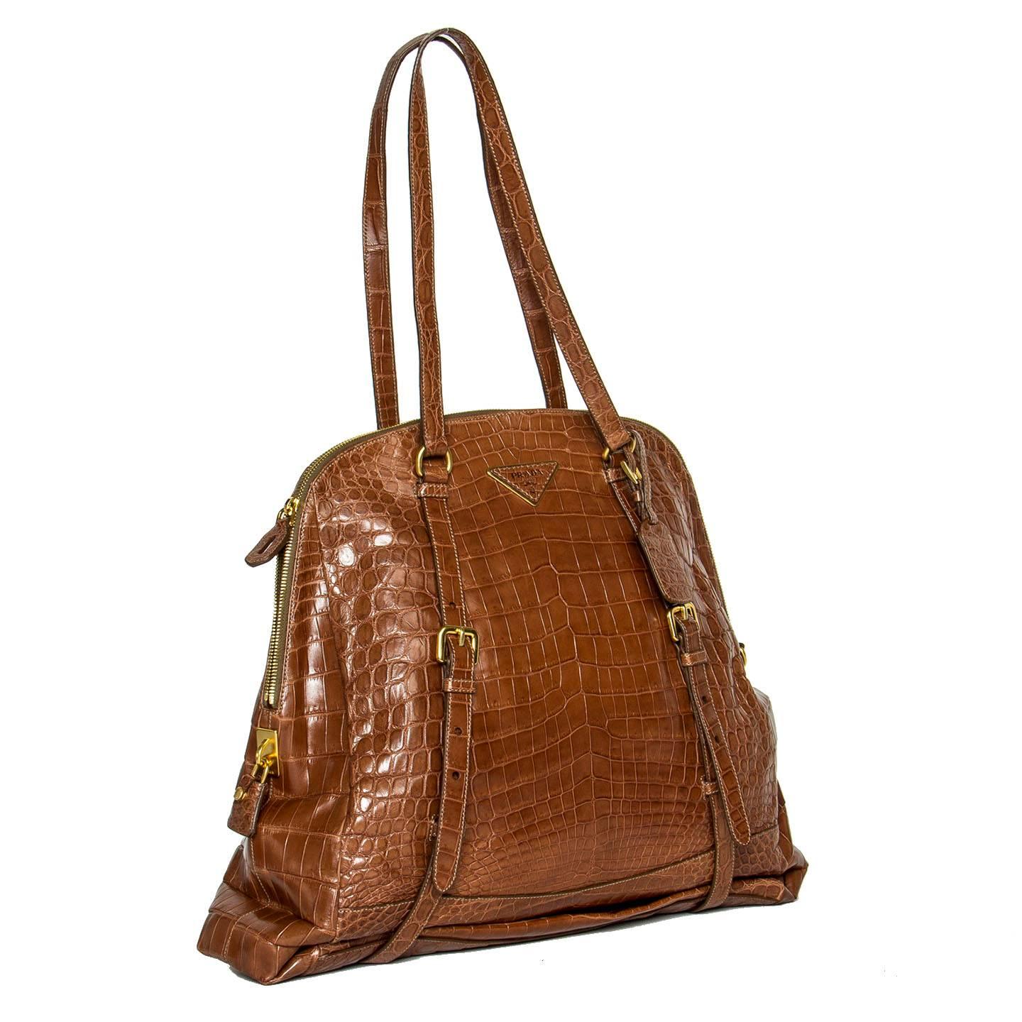 Light brown crocodile large bag with long shoulder straps that go around the bag, decorate and make the length of the body extendable. All the buckles and the chunky zipper are brushed gold color, as well as the triangular metal and leather Prada