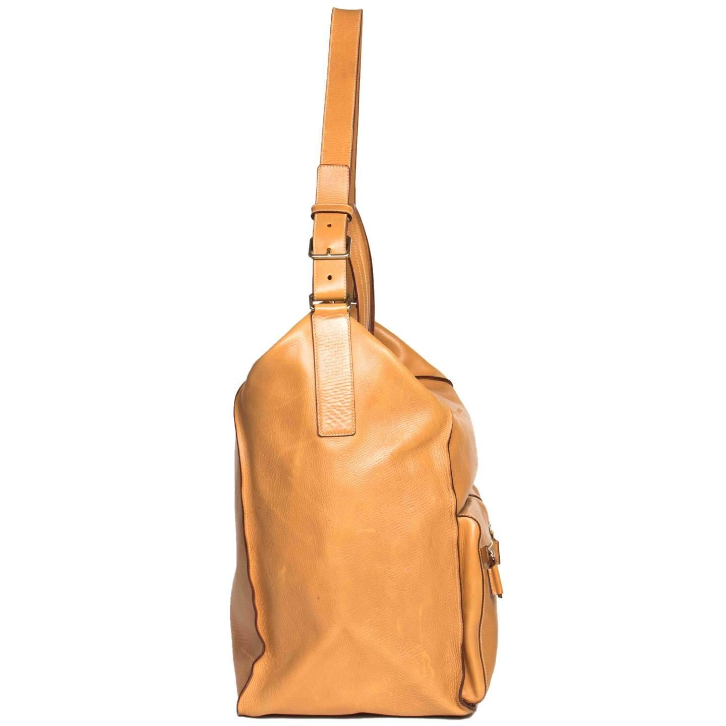 Natural textured tan colored leather large bag with a rectangular shape and camera bag style front pockets. All sections of leather are stitched together with ecru top stitches leaving the seams visible and enriched by a dark brown paint finishing.