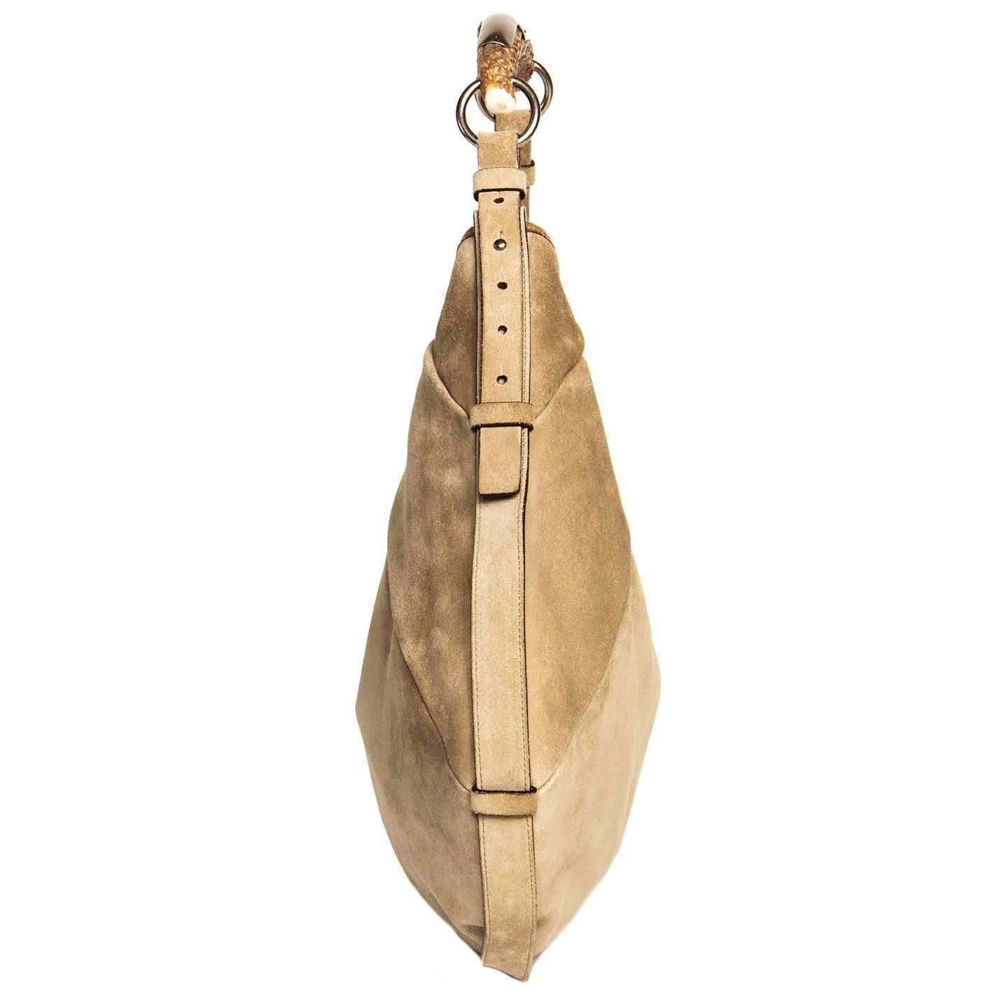 Collection taupe suede hobo medium size bag with large natural horn and brushed metal shoulder strap, attached with adjustable suede straps on both sides. A strap and loops embellish the perimeter of the bag and the edge of the opening is decorated