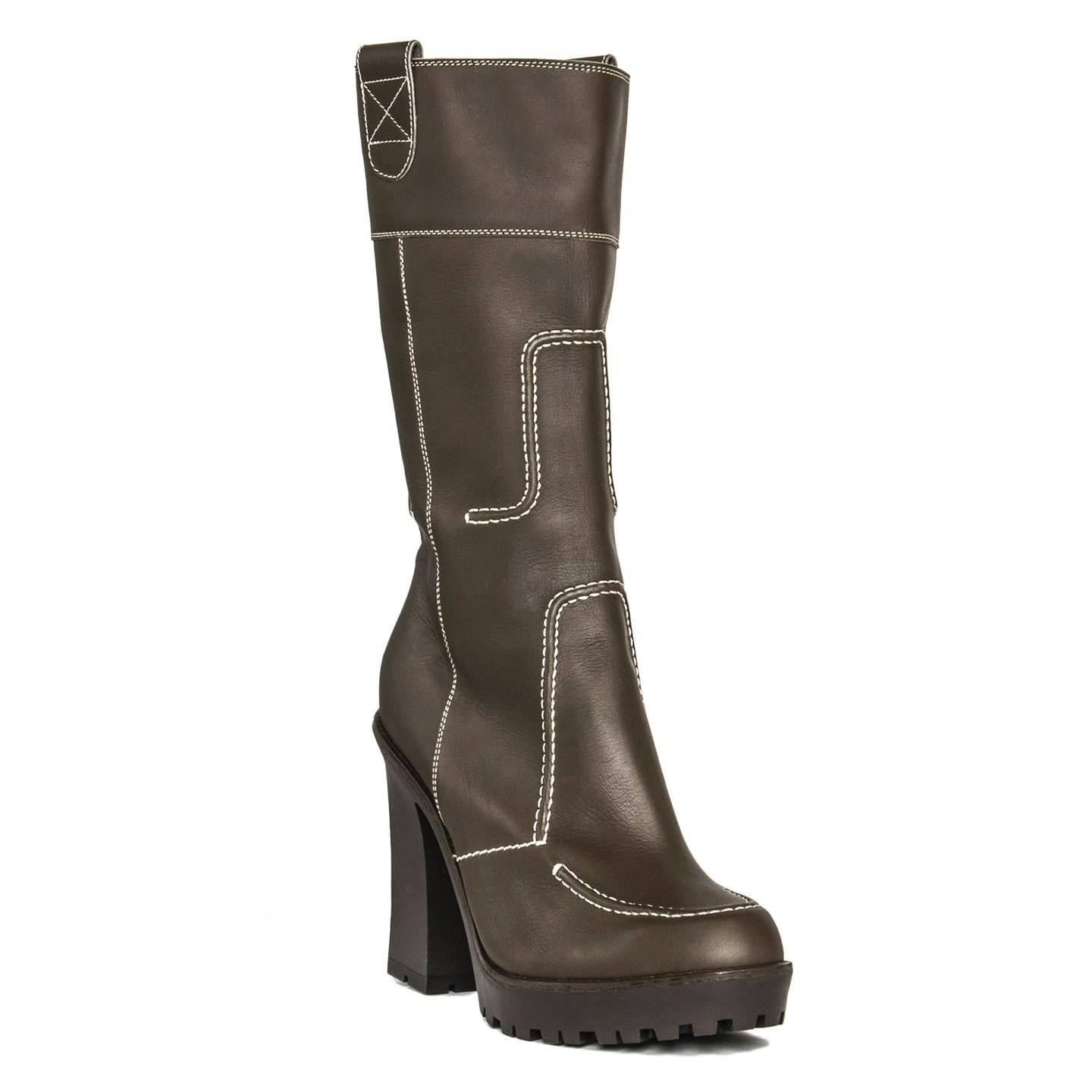 Brown leather calf high boots with platform, chunky heel and rubber sole. They have a narrow fit with a round toe shape and an instep zipper concealed by a leather flap. The main feature of the boots is the white profile stitching and geometric