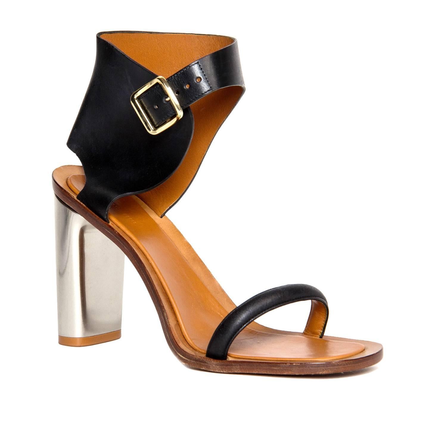 Black leather sandals fastening at ankle with a gold buckle. The sole is natural color and the chunky heel is made of silver metal. Designed by Phoebe Philo. Made in Italy. Heel 4