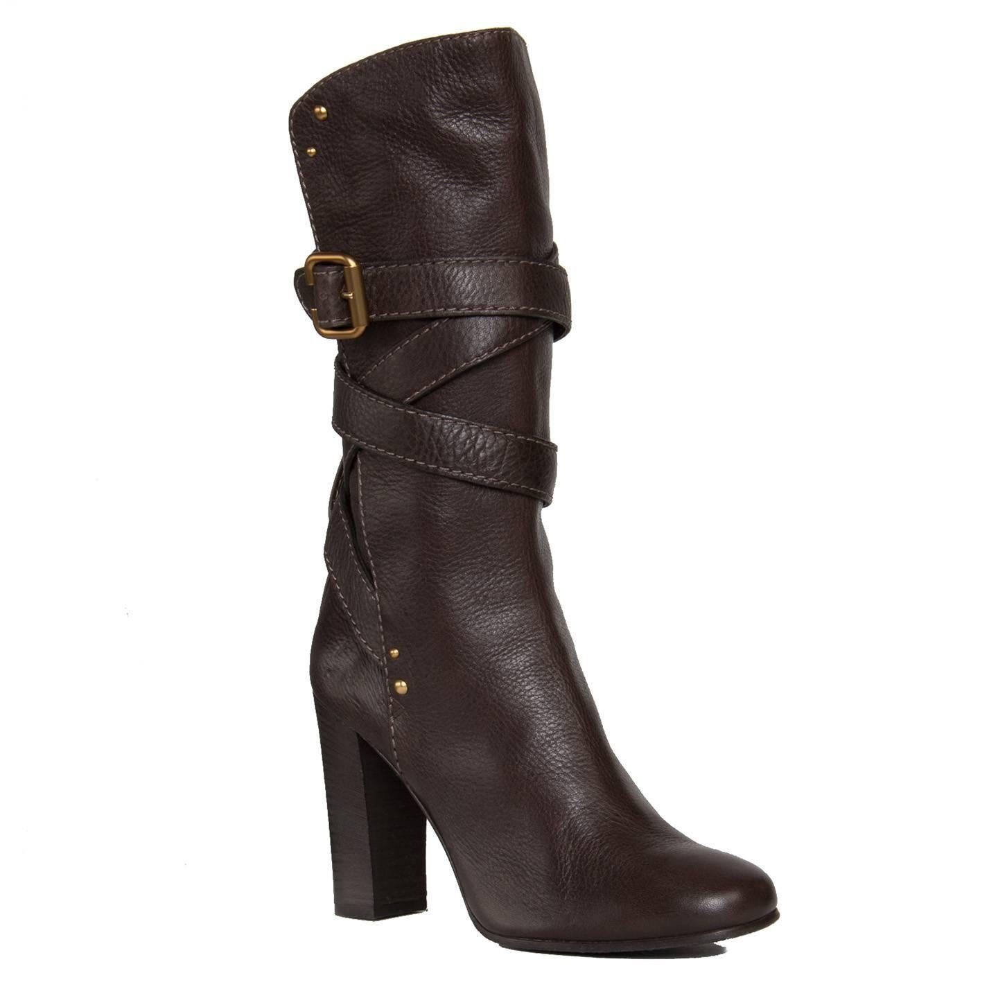 Chocolate brown calf high leather boots with round toe and wrap around straps that fastens on the side with a brushed gold color buckle. Round gold studs and thick tone-on-tone stitches decorate the boots further. Made in Italy. Heel 4