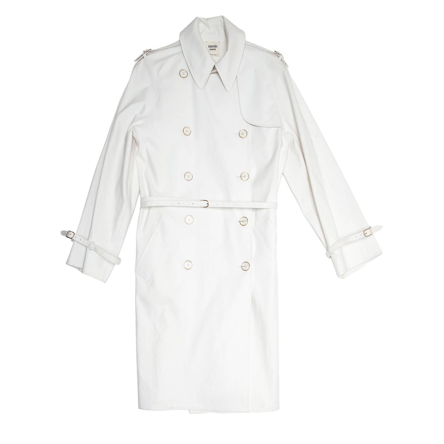 White cotton & spandex classic trench coat with thin belt that fastens with a gold small buckle. The front is double breasted and it fastens with elegant clear buttons with gold edges. The raglan sleeves are straight, quite wide and round on