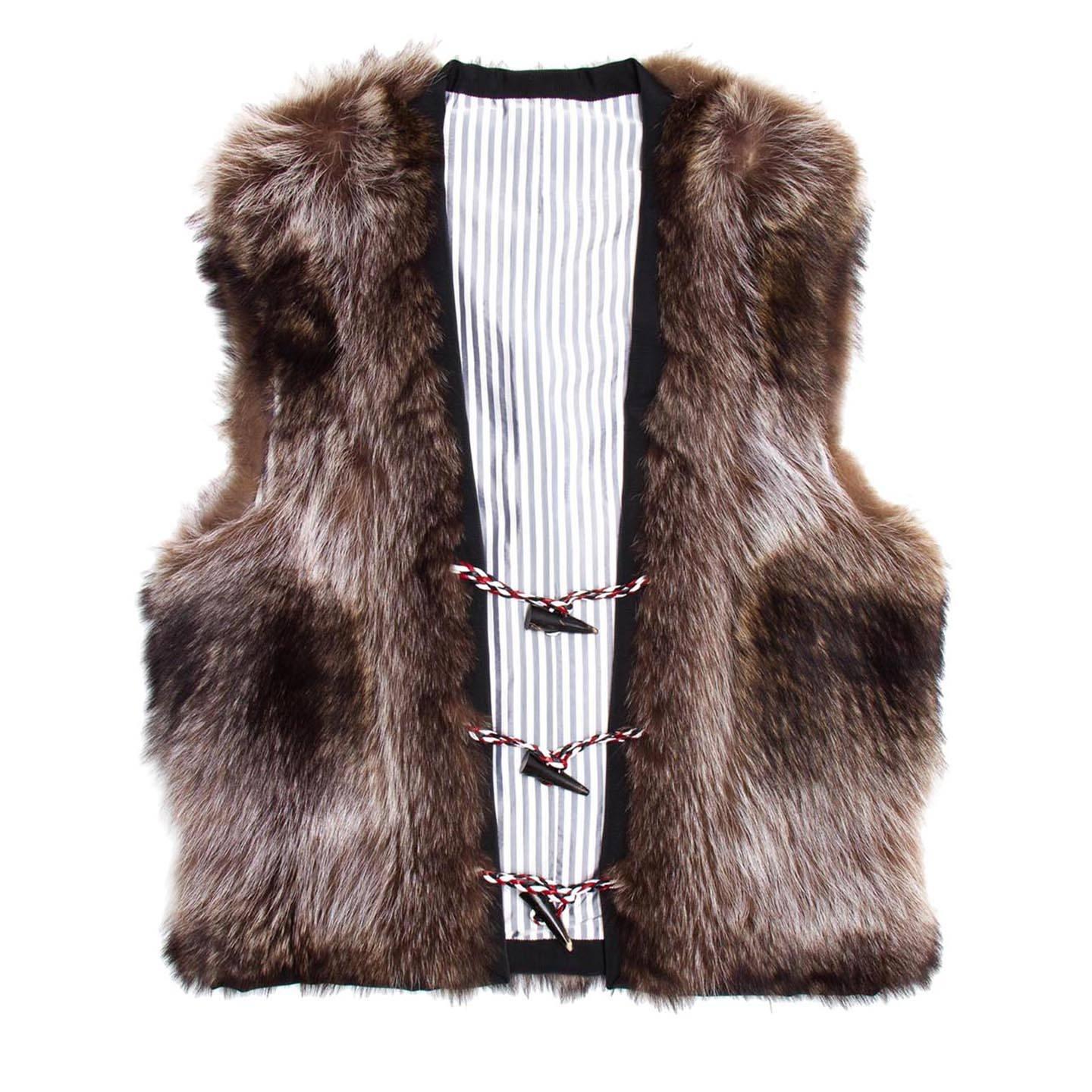 Waist length raccoon fur vest with horn toggles and red/white/blue braided leather loops closure. The profile of the vest is enriched by black grosgrain and the lining is striped white and grey. Made for Men Worn by Women too.

Size 