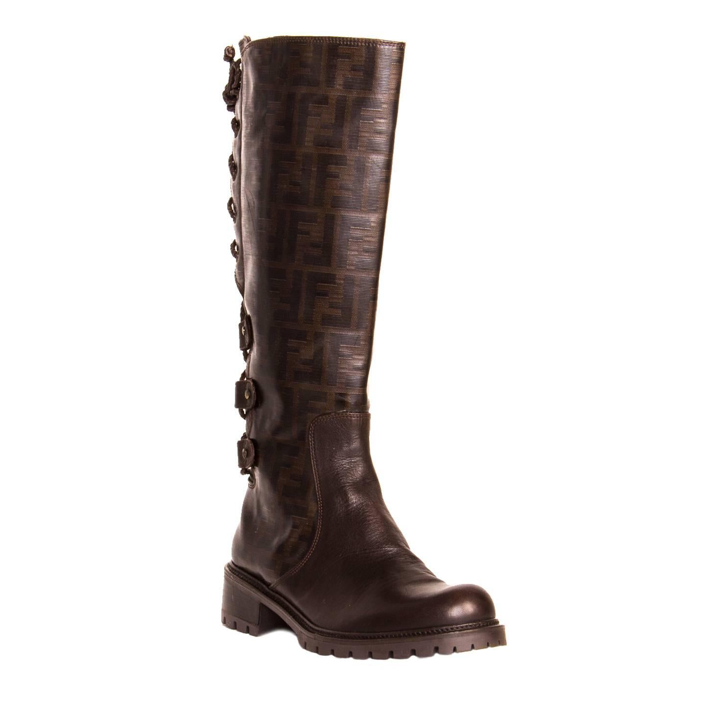 Dark brown knee high boots with Fendi logo fully printed calf and plain leather front. The back of the calfs are embellished by a leather braided lace up detail, while a bronze metal zipper is in the instep. The front is round and the rubber sole is