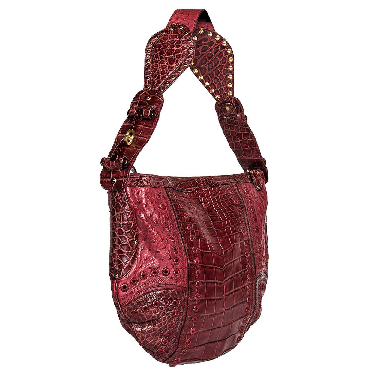 Burgundy shoulder bag made with a stunning crocodile and ostrich patchwork. The bag is adorned by embroidered little holes that follow the patch profiles. The wide shoulder strap has small round studs and is also enriched by a unique jewelry buckle