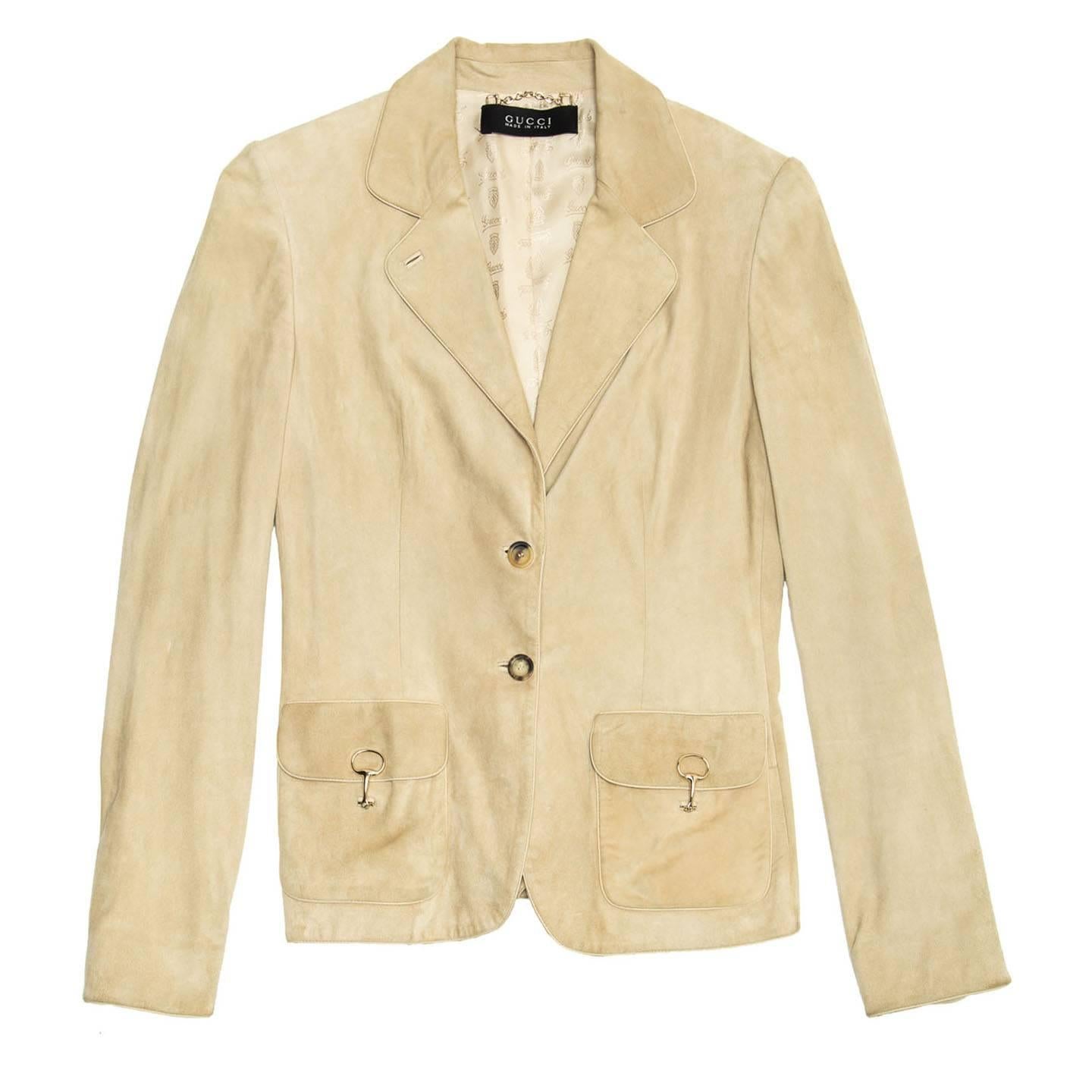 Beige suede jacket that fastens on front with two horn buttons. The lapel is of a medium size embellished with tone-on-tone leather piping to match hem and cuffs that are also characterized by a little vent with round profiles. The patch pockets are