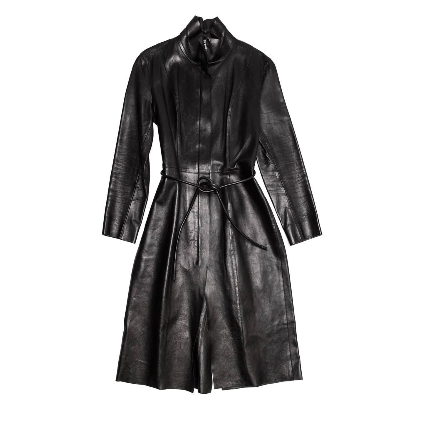This black leather coat is a composition of very clean and elegant panels with raw edge finishing and top stitched together. The standing collar has a raw edge cut too, there is no lining and the front opening fastens with a black metallic open