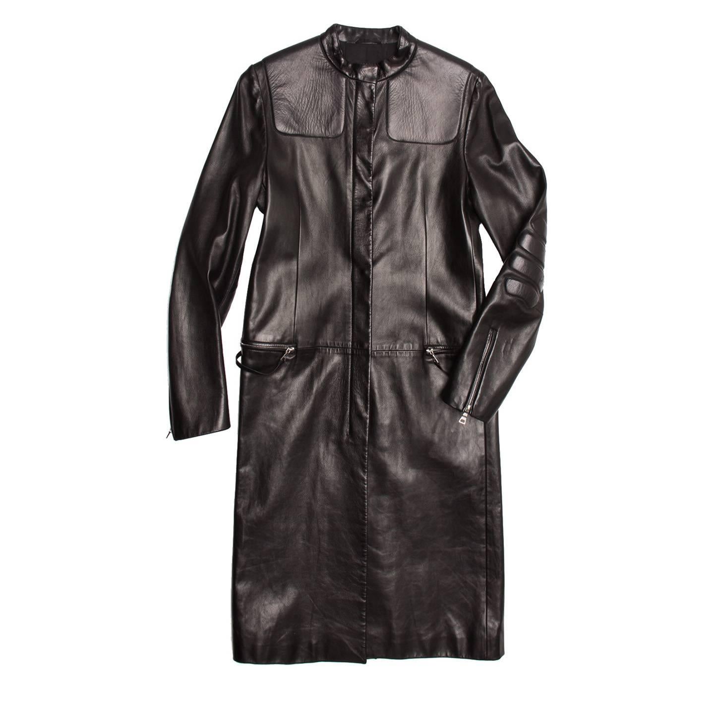 Long black sleek leather moto-racer coat with a futuristic feel. Zippered pockets at waist seam with self leather fixed pulls. Mandarin collar and hidden snaps at front placket. Raised lightly padded detailing at elbow area with zippered back cuffs