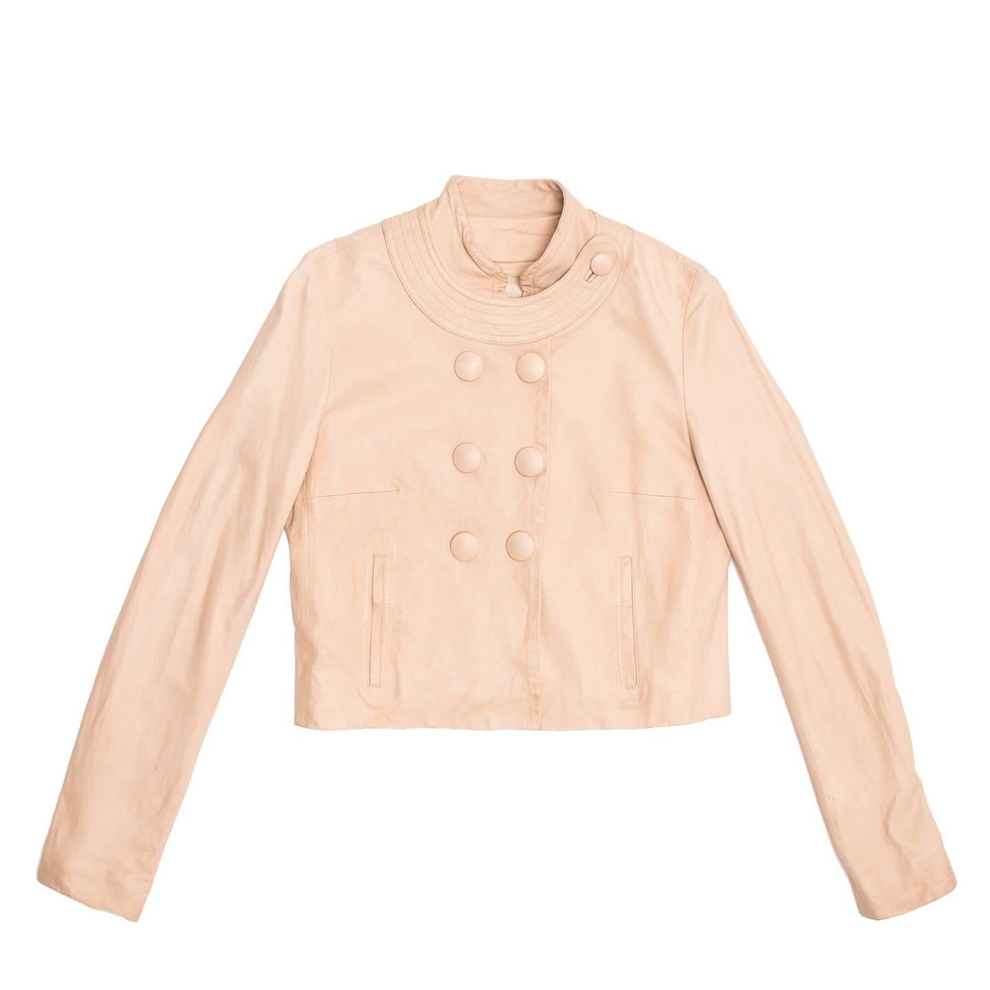 Pale pink lambskin jacket with mandarin collar. Under the standing collar a round one is applied and closes on the left shoulder with a leather covered button to match the bigger ones of the double breast closure. The bottom collar is enriched with