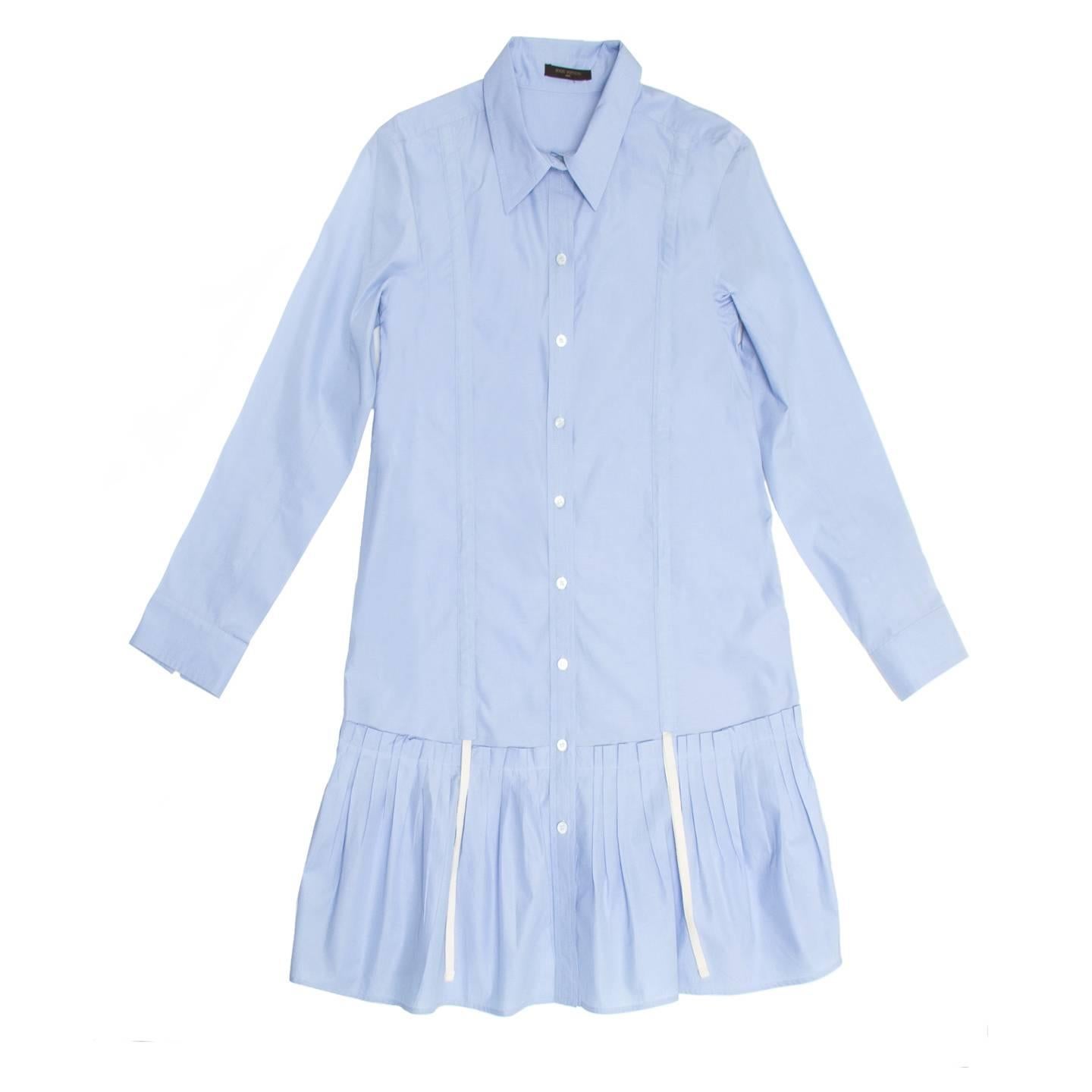 Sky blue cotton knee length shirt dress with a pleated drop waist skirt part. The fit is straight and the front opens from neck to hem, the collar is pointed peter pan style and the sleeves are long. Drawstring detail enrich the side seams and front