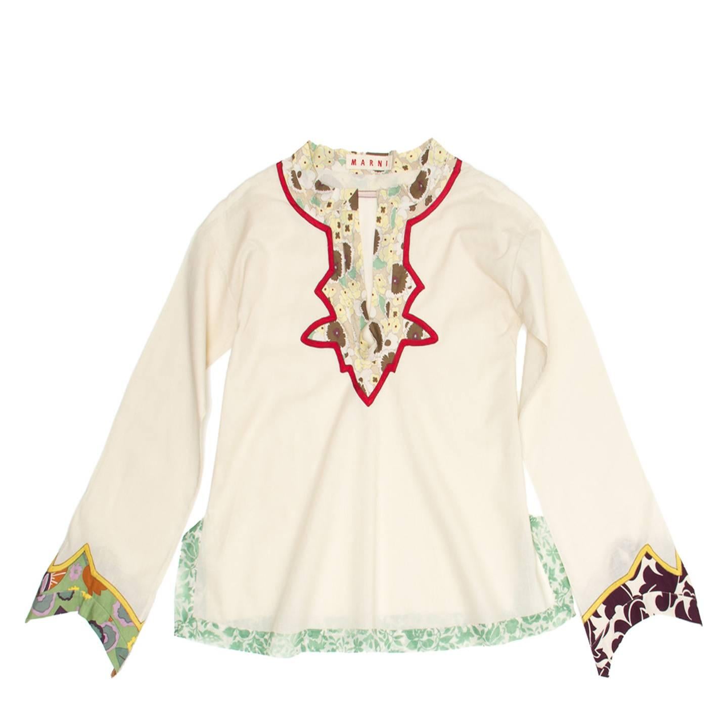 Cream cotton tunic top with long sleeves, below hip length and Indian motif floral details. The neckline is enriched by a small floral print standing collar and inserts with a red profile around neck and front opening. The body part has a slight