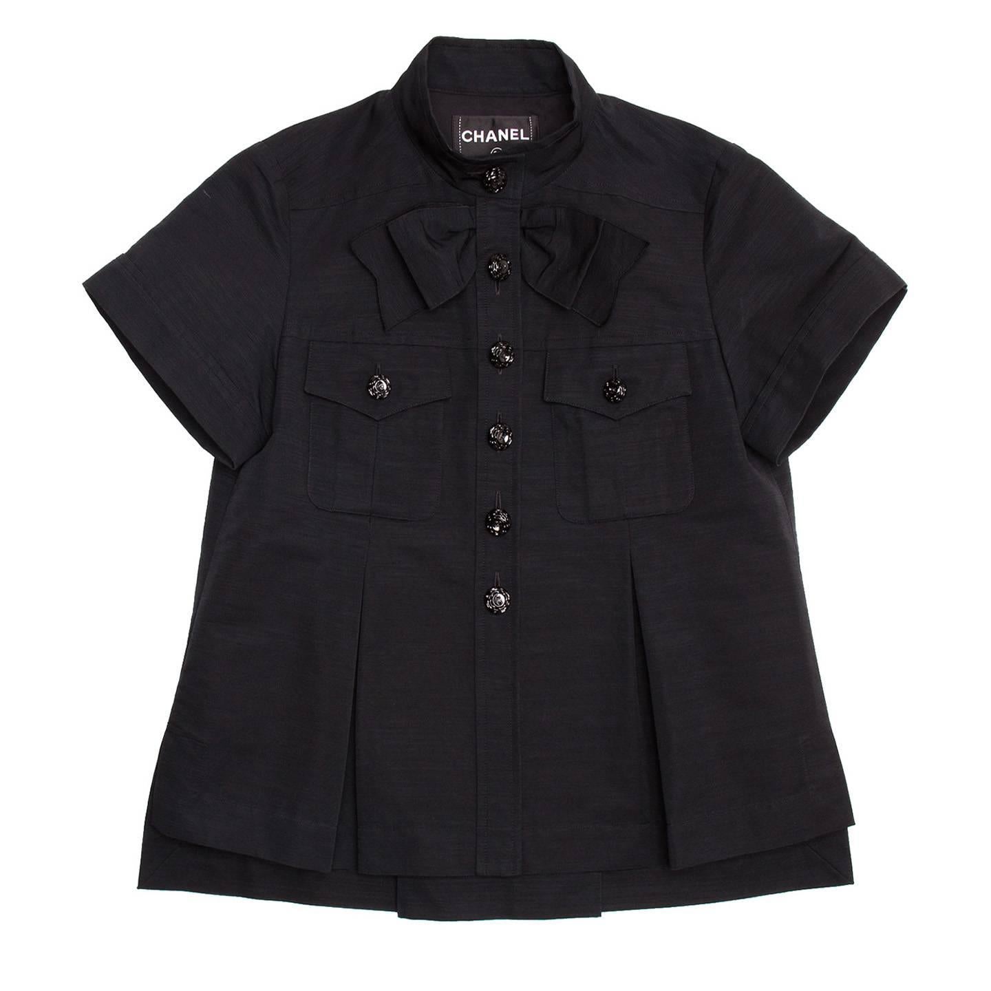 Black ribbed cotton shirt jacket style. Hip length cropped style with bow detail under the Nehru collar and pockets at top front embellished by beautiful Chanel logo black metal buttons. Front and back inverted pleats emphasize the A-line