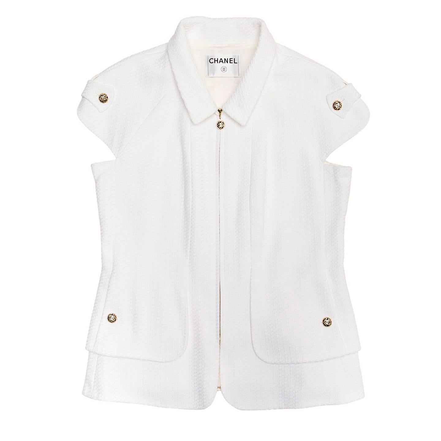 WHite thick pique cotton jacket with a peter pan collar and cap sleeves enriched by a rounded slit and a self-fabric strap attached with brushed gold Chanel buttons. The hem has two layers rounded at front, two slit pockets sit on the shorter one