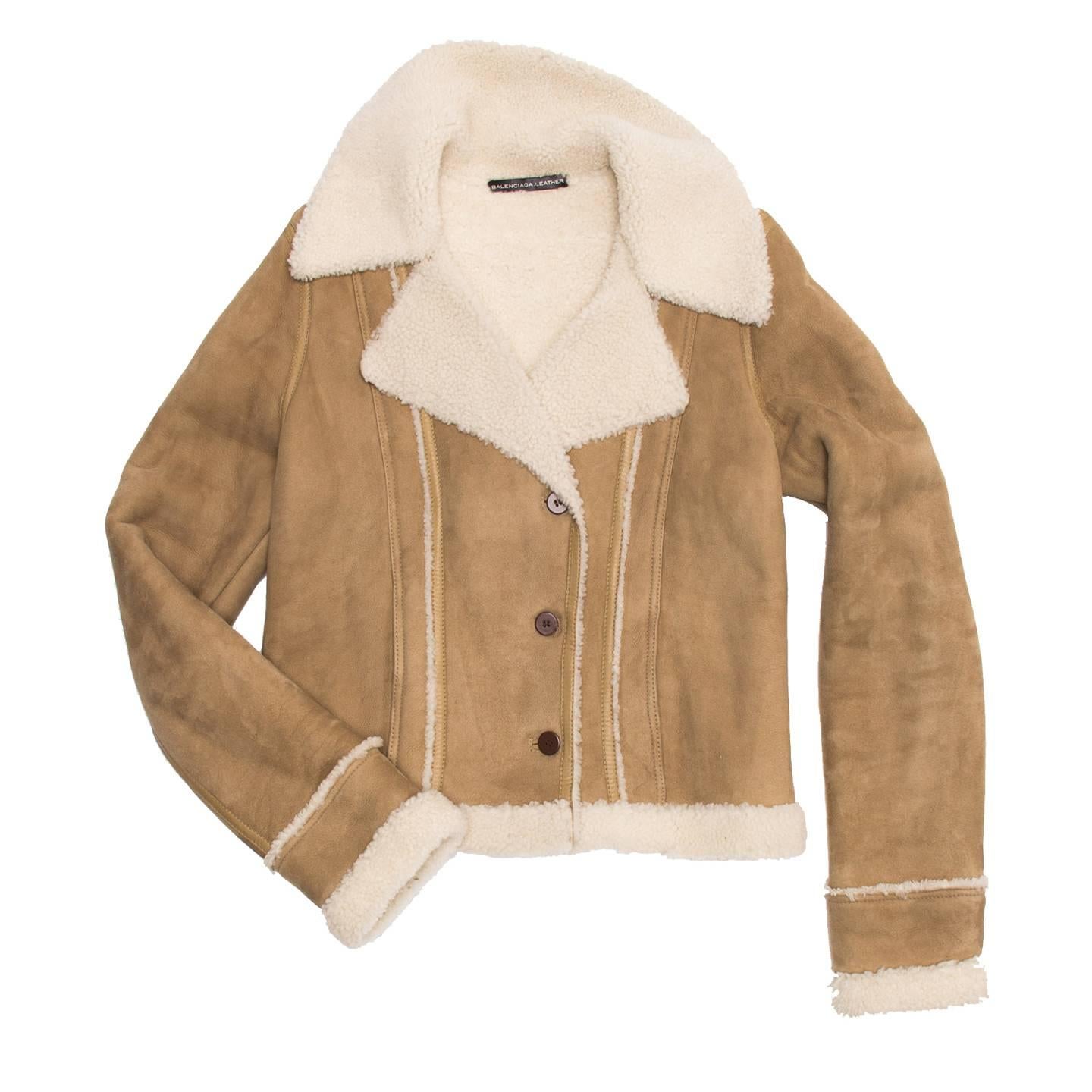 Lambskin suede cropped jacket with shearling lining, collar, cuffs, hem and seam details. The fit is quite tight thanks to the front and back darts that are emphasized by a leather tape and white shearling. The front has a small double breast
