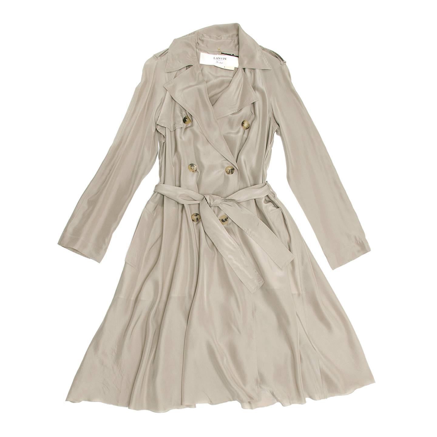 Silk taupe tent shape trench coat with narrow shoulders, very flared hem, knee length and ribbon belted waist. A deep inverted pleat at back create a larger volume, the waist is tighten by a tone-on-tone belt and the double breasted front fastens