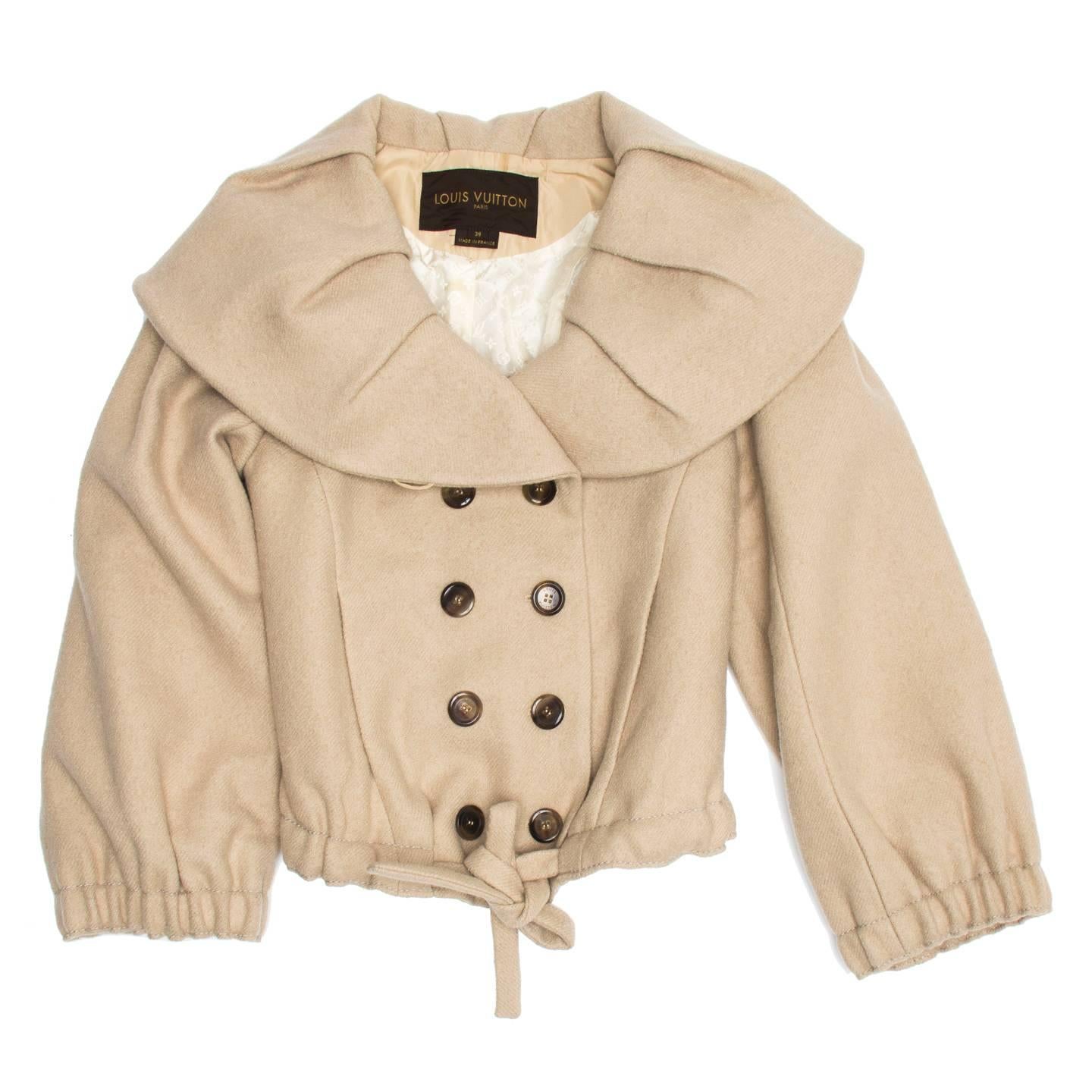 Beige wool and mohair blend cropped jacket with double breast opening and shawl collar. The collar is wide and adorned with fixed pleats while the cuffs are gathered as well as the the hem at front, which also has a self-fabric tie. Slash pockets