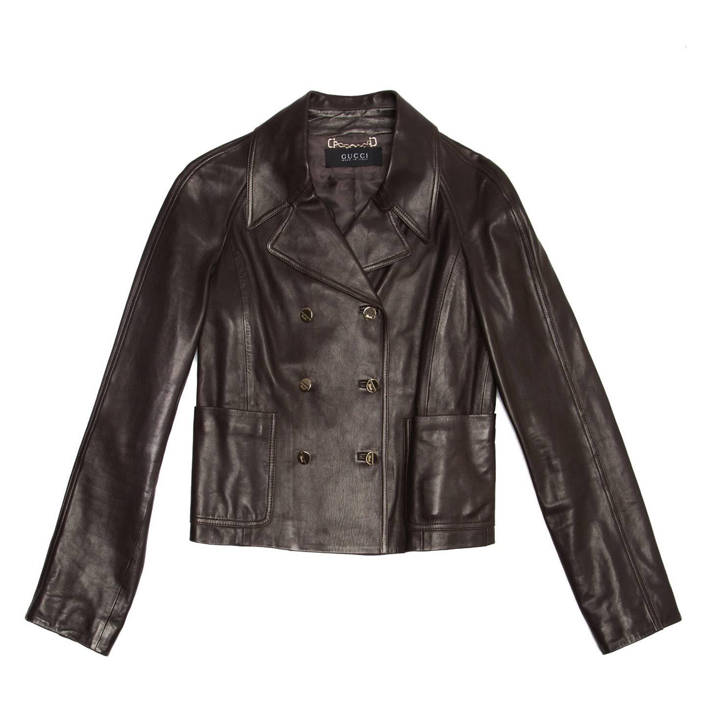 Dark brown soft leather cropped jacket with small lapel, front patch pockets and back belt. The double breasted closure and the cuffs opening fastens with Gucci logo silver metal buttons. The brown inner lining is embellished with tone-on-tone